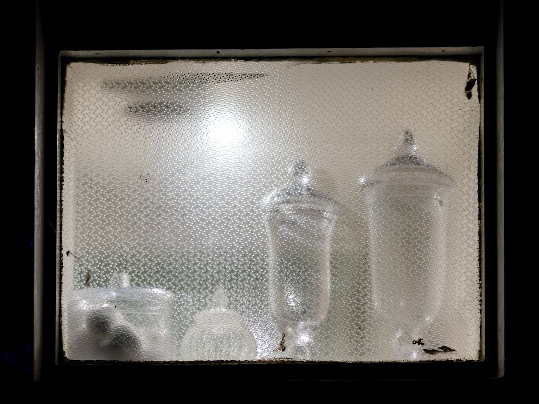 Fuktskadat källarfönster med otydliga silhuetter av glasbehållare.