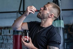 Man tar en kapsel från en burk med aminosyratillskott på ett gym.