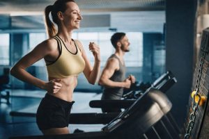 Två personer tränar på löpband i ett gym, framhäver träningsutrustning.